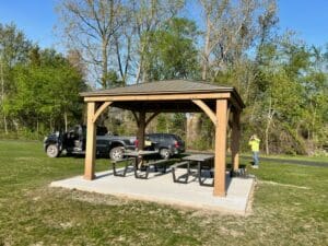 A picnic table and bench in the shade of a pavilion.