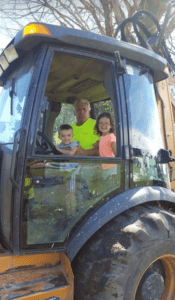 A man and two children in the cab of a tractor.