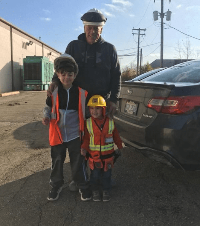 A man and two children standing in front of a car.